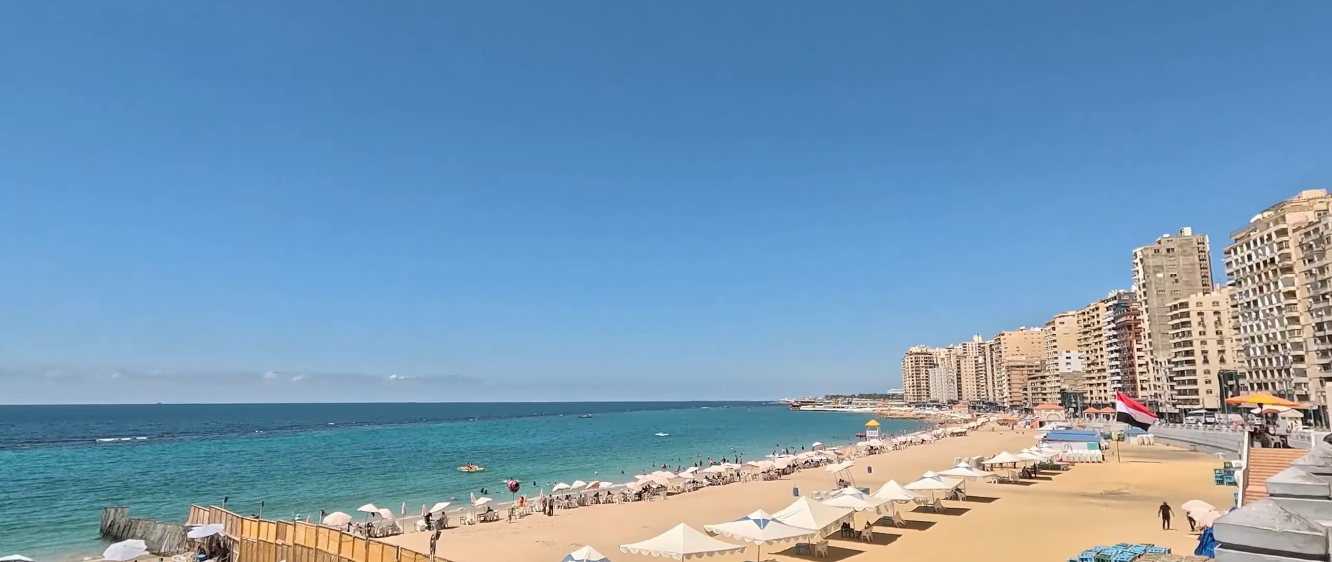 Spiaggia urbana del Corniche di Alessandria con ombrelloni e palazzi sul Mediterraneo