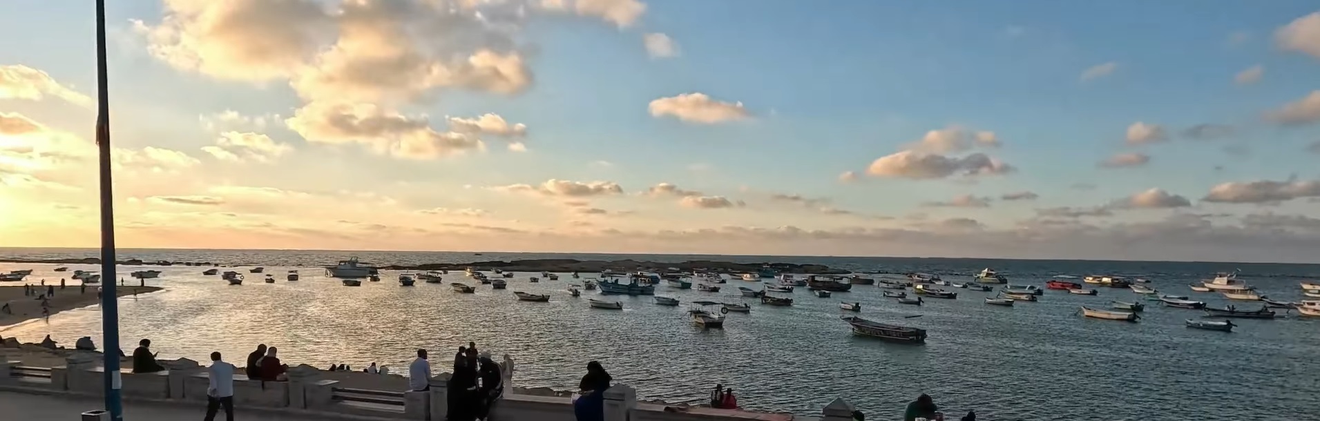 Barche da pesca in un porto di Alessandria al tramonto con persone sul muraglione