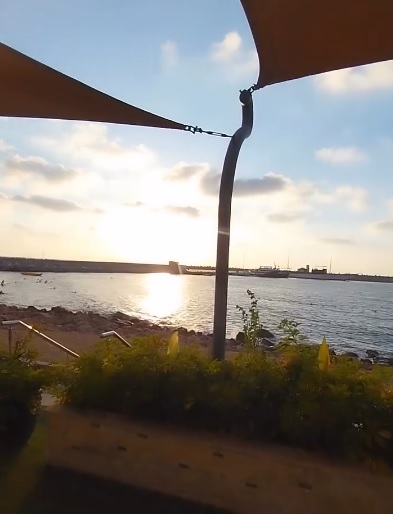 Balkonterrasse mit Sonnensegeln und Pflanzen vor ruhigem Meer bei Sonnenuntergang