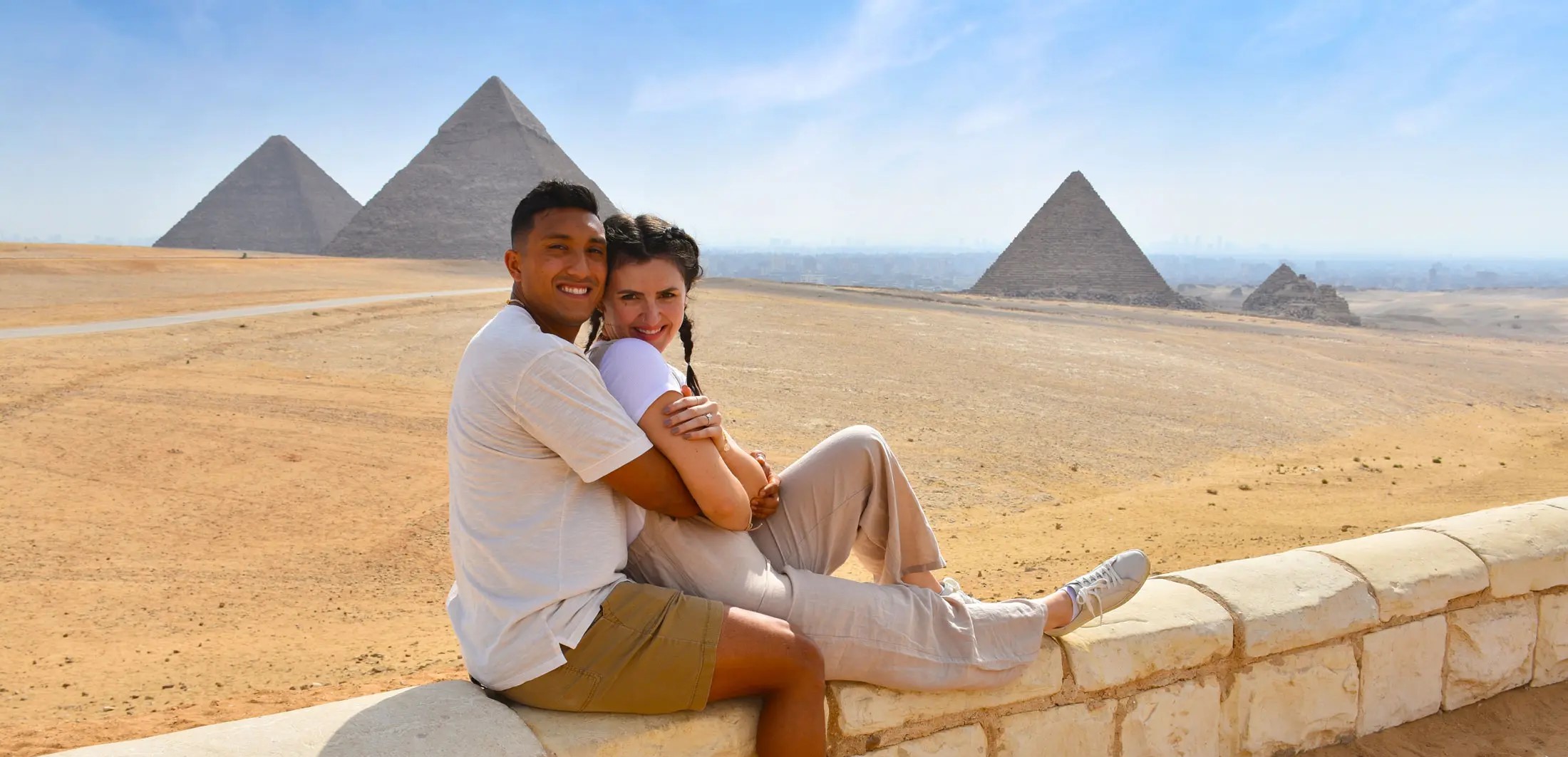 Ein glückliches Paar sitzt vor dem Panorama der Pyramiden von Gizeh in Ägypten