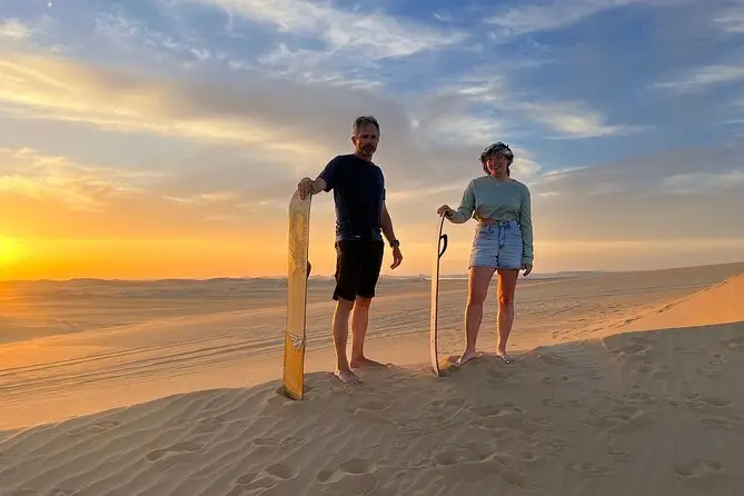 Zwei Personen mit Sandboards in der Wüste bei Sonnenuntergang