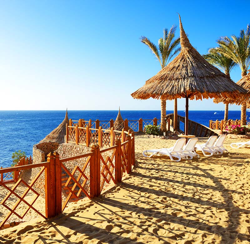 Spiaggia tropicale con ombrelloni di paglia, lettini prendisole e mare blu al tramonto.