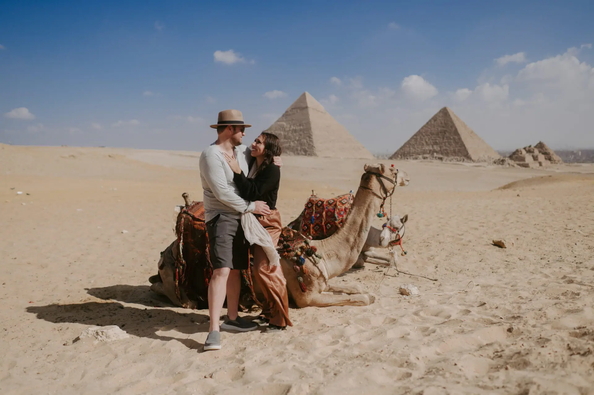 Paar umarmt sich neben einem Kamel vor den Pyramiden von Gizeh