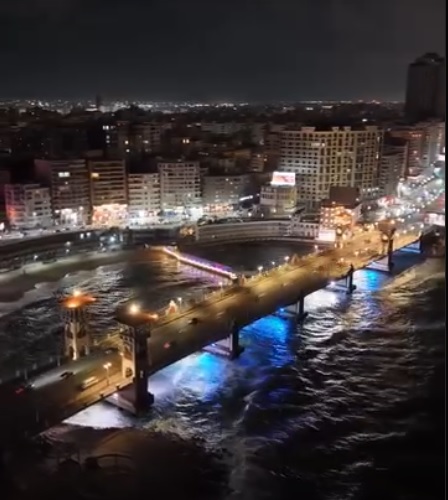 Nächtliche Luftaufnahme der Stanley-Brücke in Alexandria mit beleuchteten Wellen.