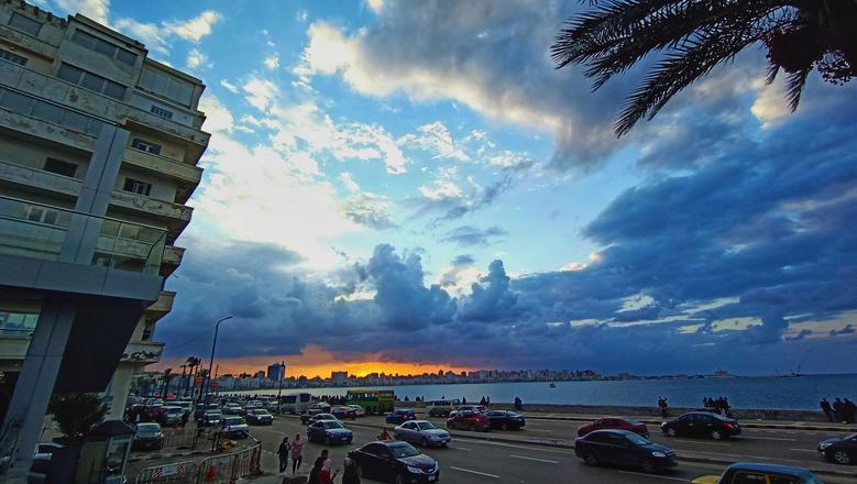 Traffico sulla Corniche di Alessandria durante un tramonto sul mare.