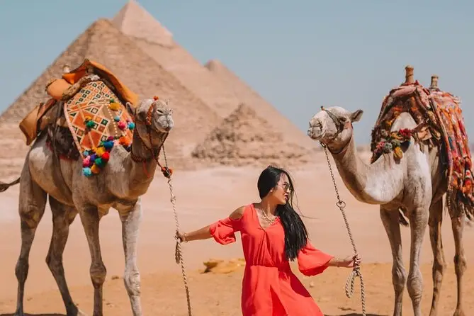 Gizeh-Pyramidentour: Eine Frau im roten Kleid mit zwei Kamelen vor den Pyramiden nahe Kairo.
