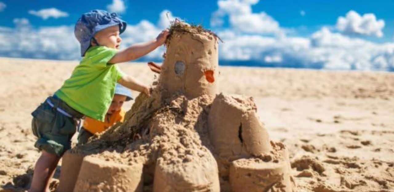 Due bambini piccoli con cappelli da sole che fanno un castello disabbia sulla spiaggia