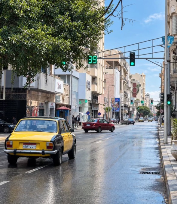 Clásico taxi amarillo y negro conduciendo por una calle mojada de Alejandría.