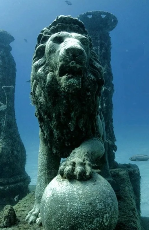 Statua di leone sommersa che poggia la zampa su una sfera di pietra.