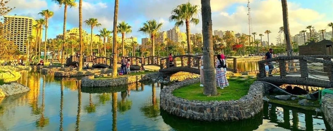 Artificial lake with stone borders, wooden bridges, and palm trees in Antoniades Gardens.