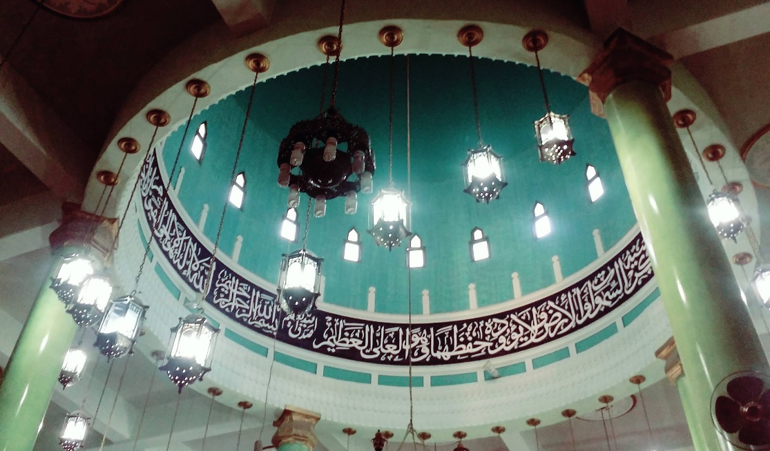 • Green interior dome of the mosque with Arabic calligraphy and hanging lanterns.
