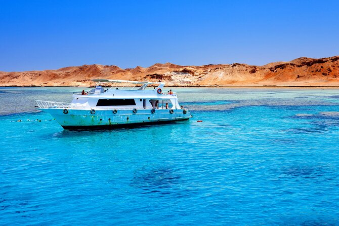 Barco navegando por las aguas cristalinas del Mar Rojo con montañas desérticas al fondo.