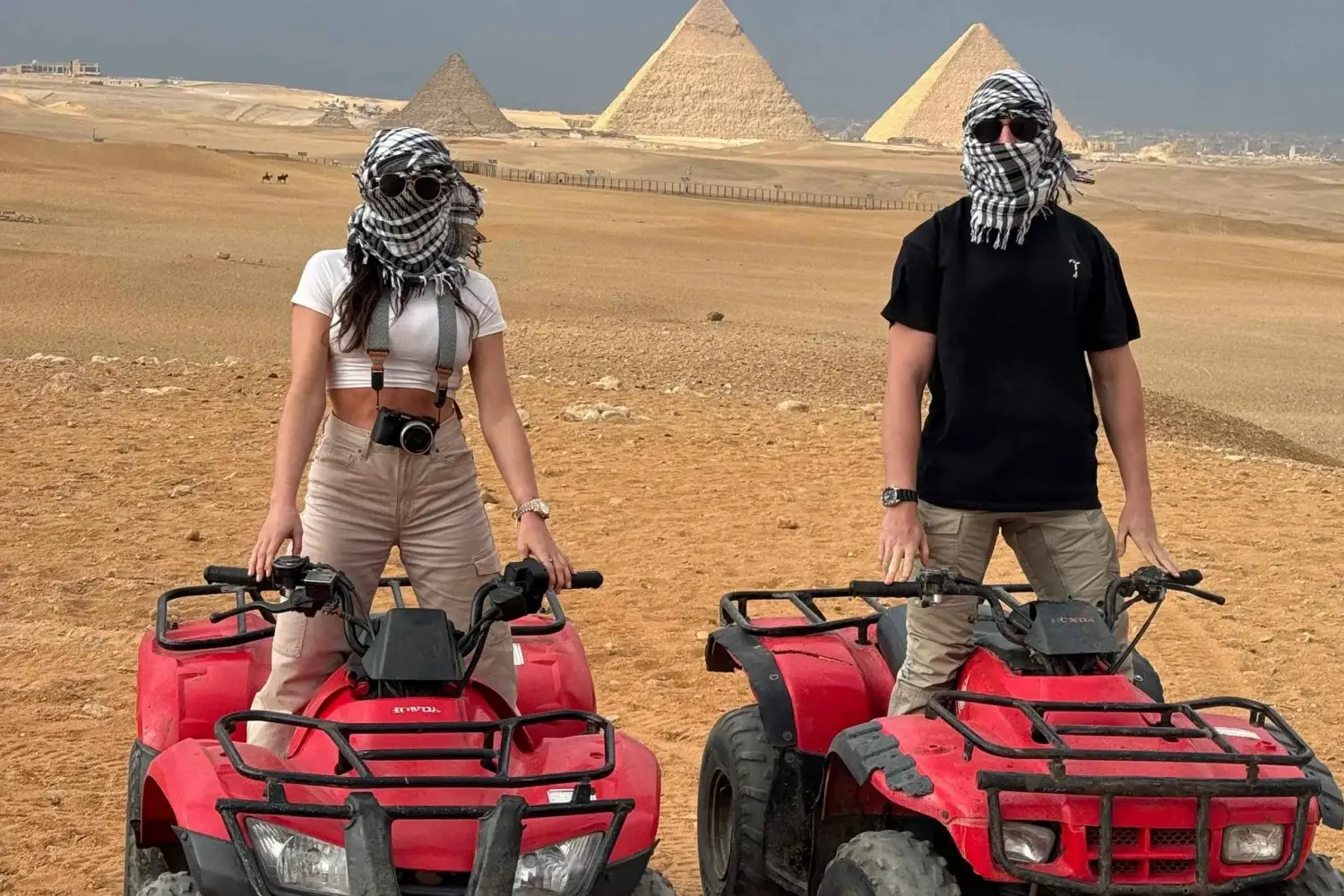 Dos visitantes en quads durante una excursión por el desierto con las Pirámides de Giza al fondo