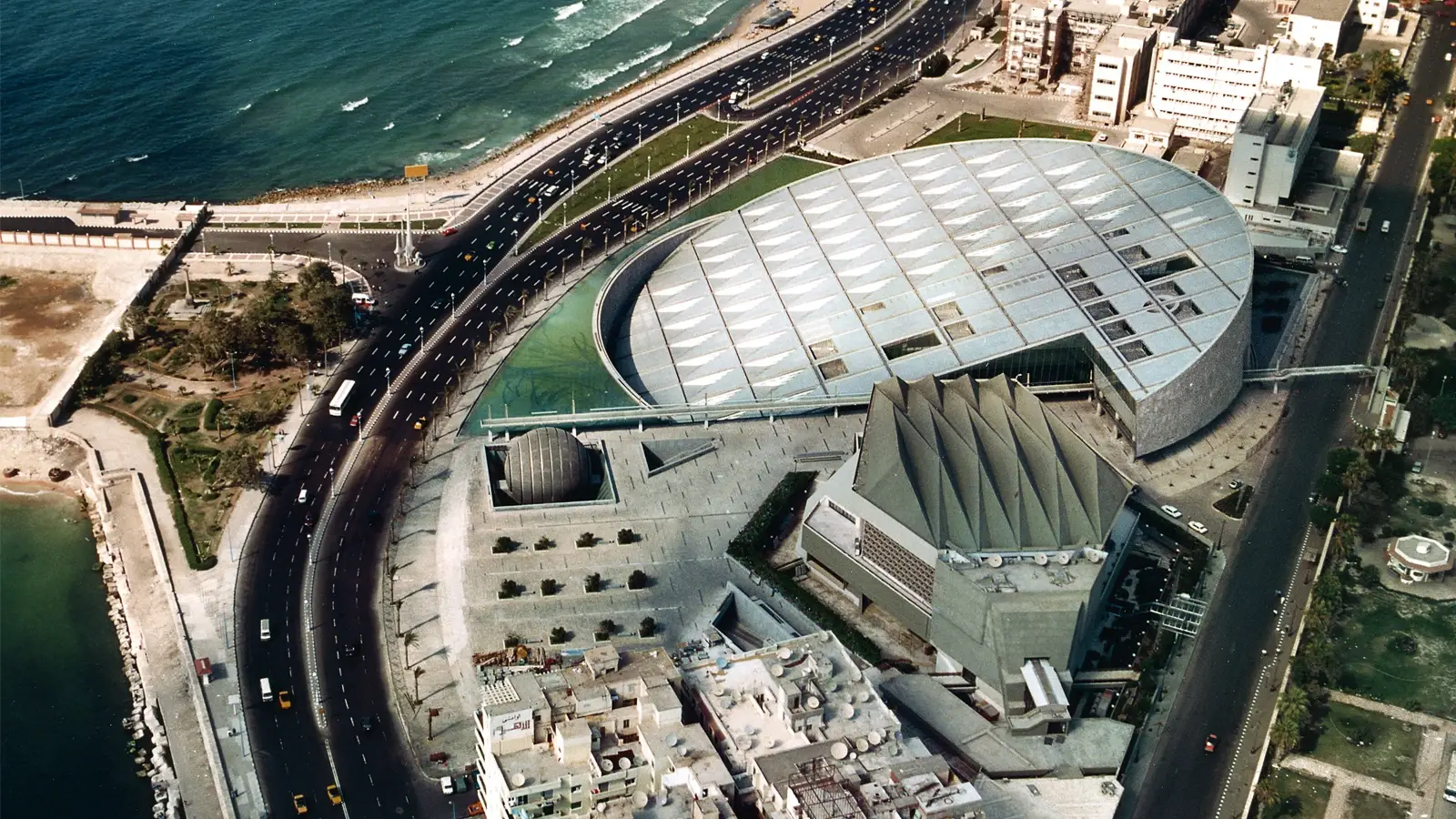 Luftaufnahme der Bibliotheca Alexandrina mit geschwungenem Dach und Uferpromenade
