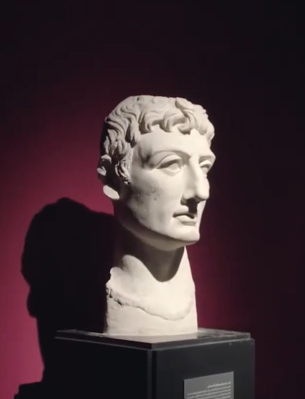Ein marmorner Statuenkopf vor einer dunkelroten Wand im Museum